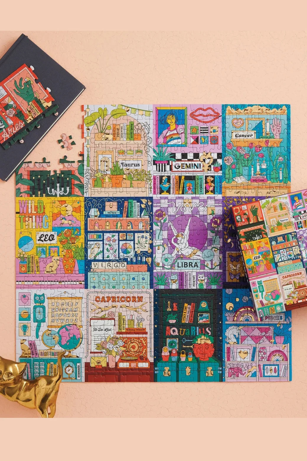 A set of colorful jigsaw puzzles arranged on a peach background, featuring astrology illustrations such as Libra, Capricorn, and gemini. A black notebook and a small gold figurine are styled as props.