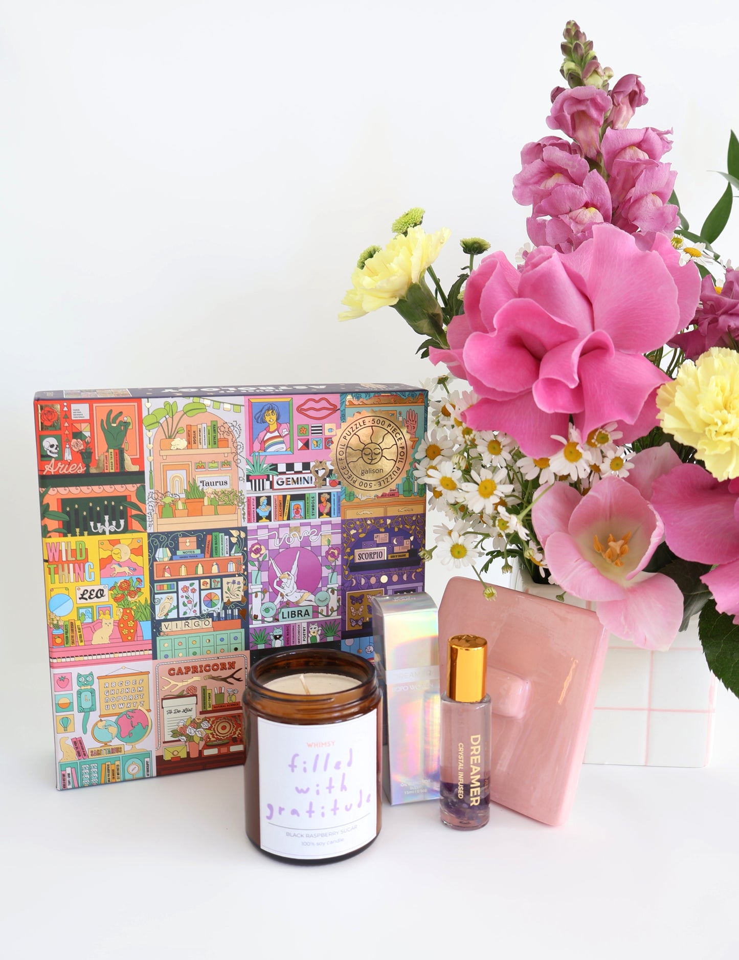 A curated gift set featuring a colorful Zodiac sign puzzle, a  gratitude candle, a colourful fresh flower arrangement styled in ceramic vessel with lid with colourful fresh flowers to keep your trinket in afterwards!